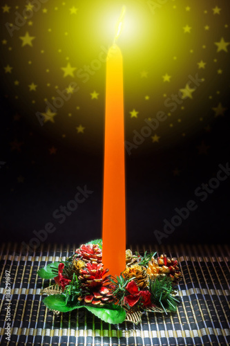 The orange candle on the table with Christmas decoration.