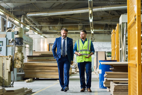 Full length portrait of young workman giving tour of modern factory to handsome mature businessman discussing possible investment, copy space