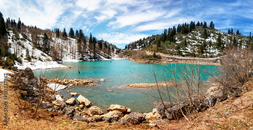 Panoramic view of Frozen crystal blue lake and snowy woodland in winter Georgia. Shaori lake, Racha. Caucasus. Colorful vibrant outdoors