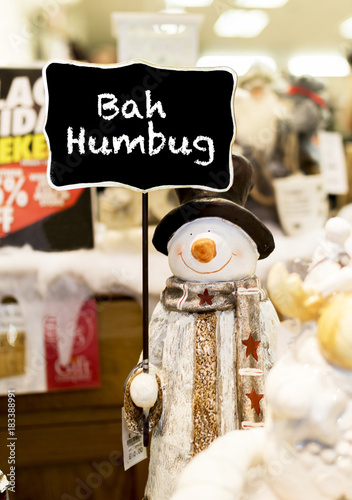 Ornamental snowman wearing a scarf, coat and a top hat holding up a Bah Humbug sign in a Christmas shop