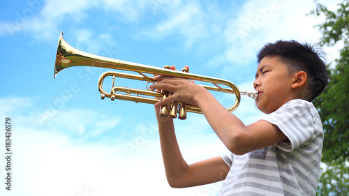 Asian boy playing trumpet with blue sky background.