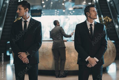 two bodyguards waiting for businessman standing at reception counter