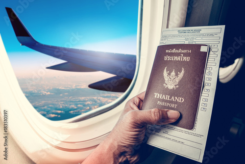 Business man holding passport and immigration form on seat next to windows on airplane vacation jorney. Hand holding passport with passport close up on plane windows background.