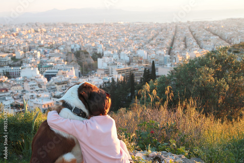 Young woman hugs her dog as they sit in a field.Athens,Greece .Real warm light from sunset.