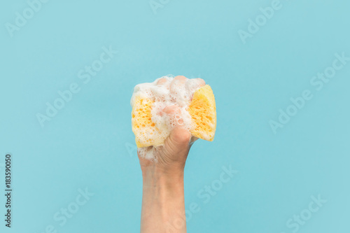 cropped view of hand holding washing sponge with foam, isolated on blue