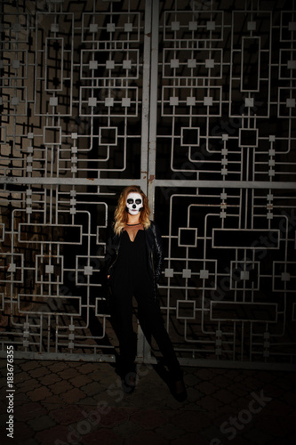 Halloween skull make up girl wear in black at night street of city against cage.