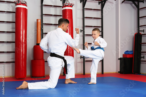 Male karate instructor training little child in dojo