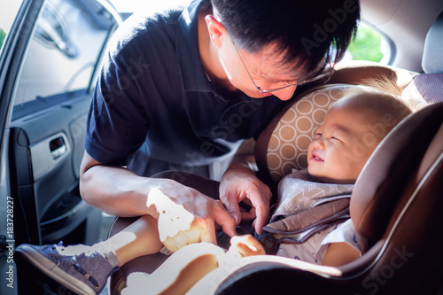 asian father helps his cute little asian 1 year old toddler baby boy child to fasten belt on car seat