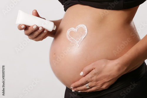  Pregnant woman applying moisturizer on belly, preventing pregnancy stretch marks