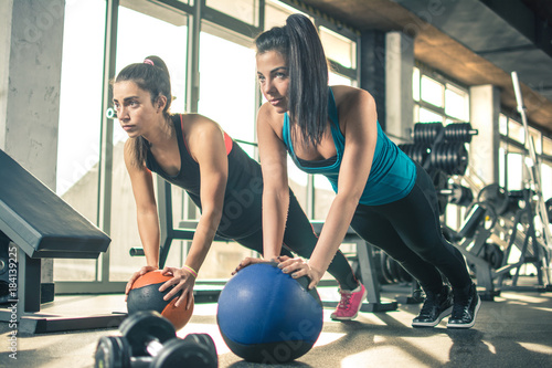 Two sporty young women exercising with pilates balls in the gym.