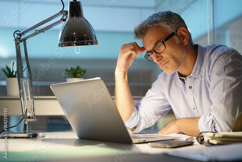 Businessman in office being thoughtful in front of laptop