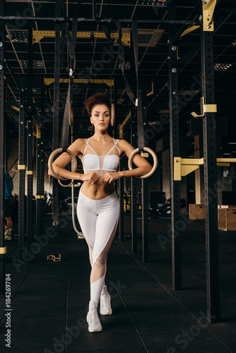 Muscular female athlete holding gymnast rings at the gym. Young caucasian woman exercising at gym with rings.