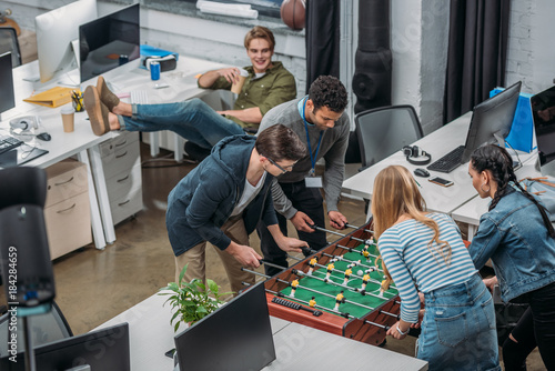 multiethnic colleagues playing in table soccer at modern office