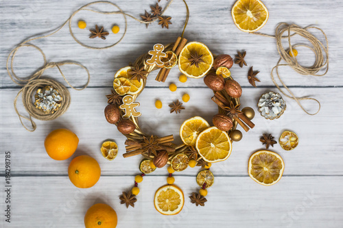 Новогодний или рождественский венок из золоченых веток, грецких орехов, палочек корицы, звездочек бадьяна или аниса, имбирного печенья в форме человечков и засушенных фруктов - лимона и апельсина
