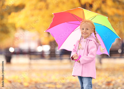 Cute little girl with rainbow umbrella in autumn park