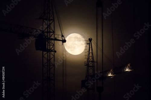 Building in the background a crane and night sky with a full moon.