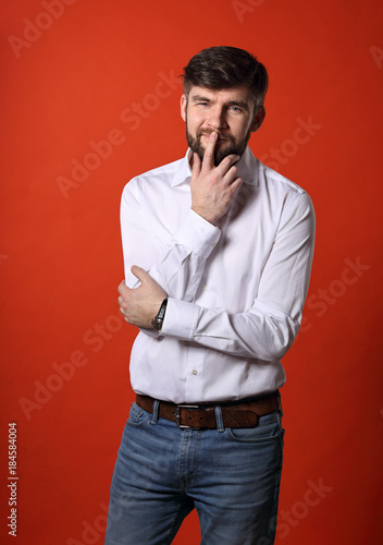 Thinking bearded charismatic man in whirt shirt looking on bright orange background. Closeup portrait