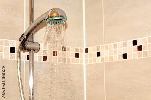 Duschkopf mit laufendem Wasser vor Duschkabine mit Mosaikfliesen
