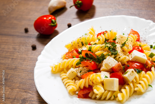 Fusilli pasta salad with cherry tomatoes and cheese in a plate on wooden table