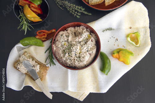 Dip from cottage cheese with sun dried tomatoes, tuna, parsley greens sprinkled with grains of black cumin, served with toast from grain bread on a black background