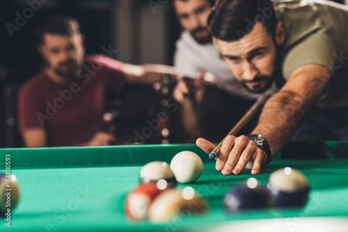 young handsome man playing in pool with friends at bar