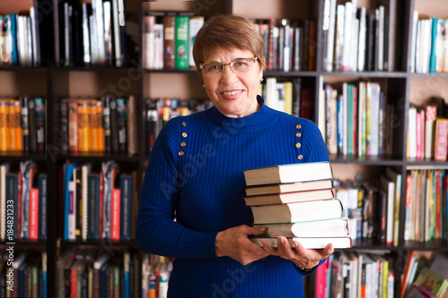 Happy senior woman with books in library.