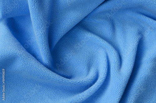 The blanket of furry blue fleece fabric. A background of light blue soft plush fleece material with a lot of relief folds