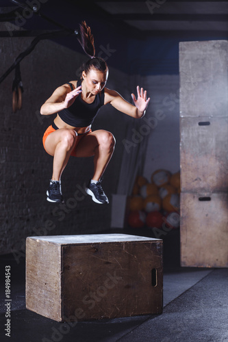 Fit young woman box jumping at cross fit gym. Female athlete doing box jumps exercise at gym