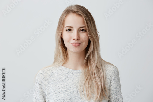Pretty smiling joyfully female with fair hair, dressed casually, looking with satisfaction at camera, being happy. Studio shot of good-looking beautiful woman isolated against blank studio wall.