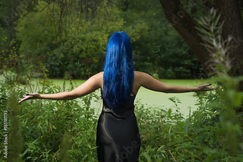 Beautiful woman with dark blue hair dressed in black dress in the magic forest