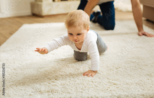 Determination. Pretty little determined child feeling glad while being at home with a kind loving father and crawling on the floor