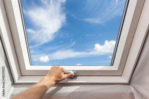 Man close new skylight (mansard window) in an attic room against blue sky