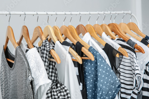 Stylish clothes hanging on wardrobe stand against light background