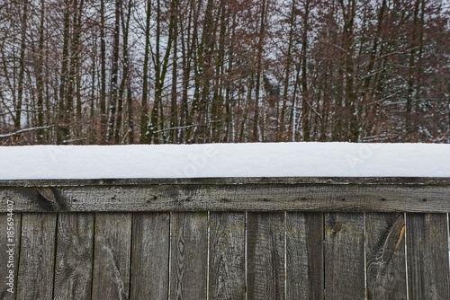 часть серого деревянного забора под снегом у деревьев