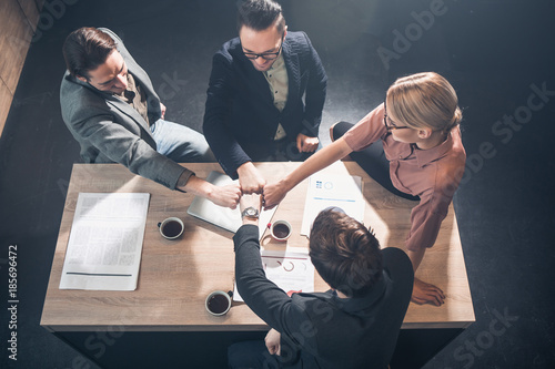 Top view cheerful female and male colleagues holding arms together while sitting at table in office. Profession and relation concept