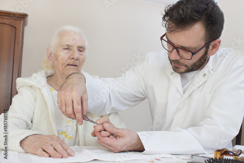 Pielęgniarz obcina paznokcie u rąk starej kobiety.
