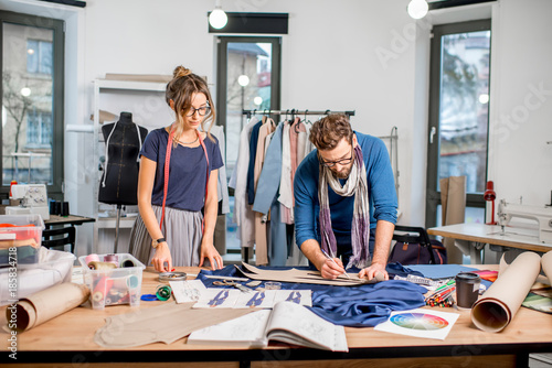 Couple of fashion designers working with fabric at the studio full of tailoring tools and equipment