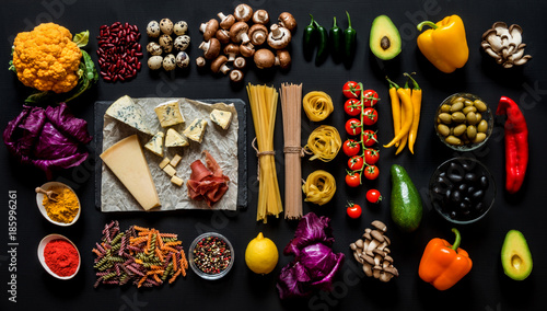 Different fresh ingredients for cooking italian pasta, spaghetti, fettuccine, fusilli and vegetables on a black background. Flat lay, top view.