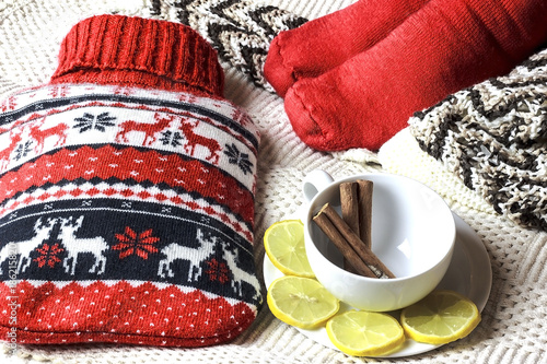 Hot water bottle, feet in warm socks,lemon slices and cinnamon sticks in a cup.