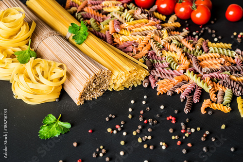 Various kind of italian raw Pasta. colorful fusilli pasta, spaghetti, fettuccine with tomatos on a black background. Closeup