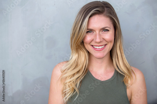 Gorgeous headshot of young bright cheerful sincere smiling caucasian blond female against a gray background