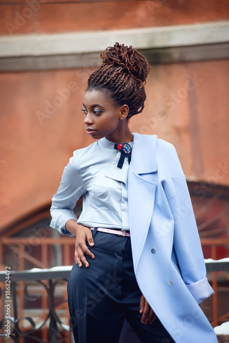 African girl with bright makeup and a blue coat stands and looks to the side on the snowy streets in style fashion