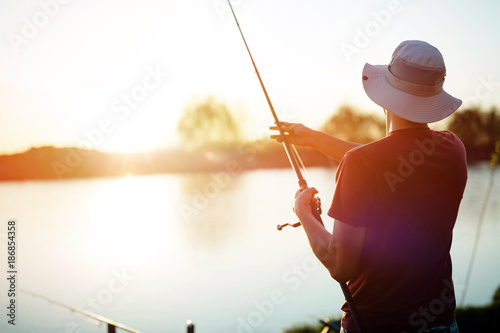 Young man fishing on a lake at sunset and enjoying hobby