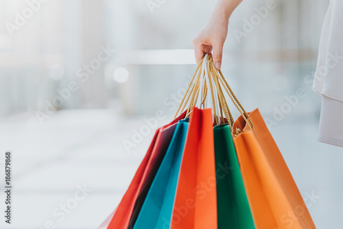 Close up shot of young woman carrying colorful shopping bags while walking in shopping mall