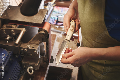 Making of a knife. Master sharpens a blade on the machine closeup in the Studio