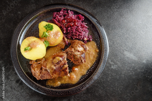 beef rolls, traditional german meal, filled meat rouladen with red cabbage, potatoes and sauce on a dark plate, dgray slate stone background with copy space