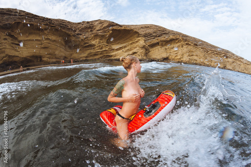 Young topless girl in thongs on pool float in ocean waves