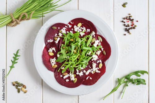 Beetroot carpaccio with rucola leaves and pumpkin seeds on wooden white background.