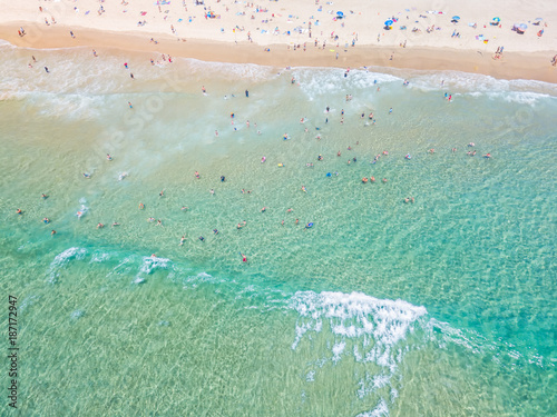 An aerial view looking down at people swimming at the beach in summer with blue water