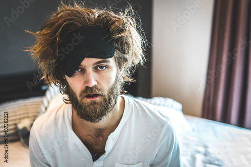 Guy sit by the bed after a night of drinking alcohol. The day after hangover and intoxitation.